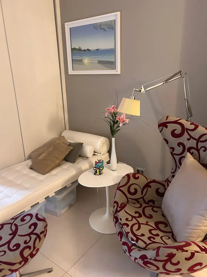 Sala de atendimento com divã branco, poltrona e luminária