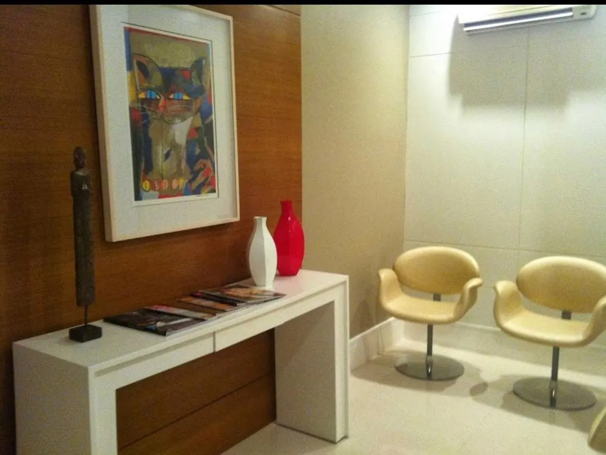 Recepção do consultório, com aparador branco, quadro e poltronas